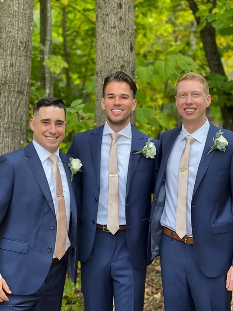 Three friends in navy suits standing outdoors at a wedding