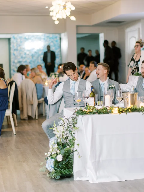 Eric wearing glasses and raising an arm while seated at a wedding reception