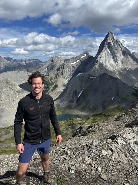 Eric pausing on a rocky ridge with a mountain peak behind him