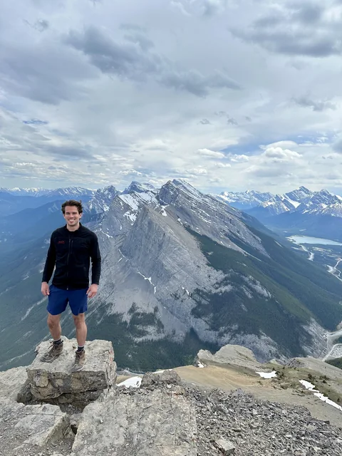 Eric standing on a rocky summit with a mountain range and valley behind him